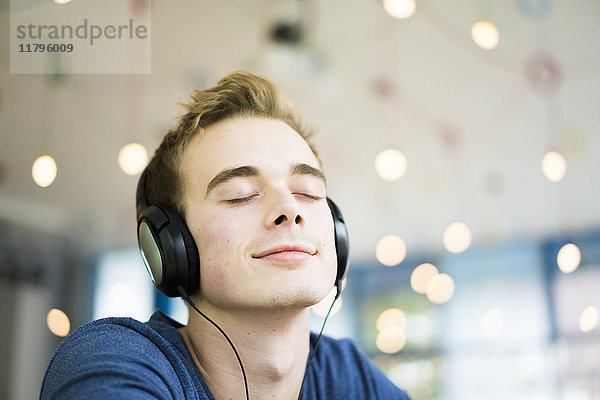 Porträt eines lächelnden jungen Mannes mit geschlossenen Augen Musik hören mit Kopfhörer