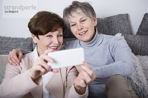 Zwei ältere Frauen  die auf der Couch sitzen und Selfies nehmen.