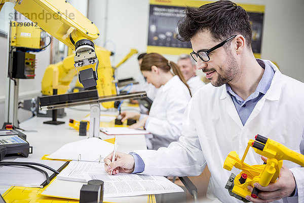 Ingenieur im Fabrikmodell eines Industrieroboters mit Notizen in der Zwischenablage