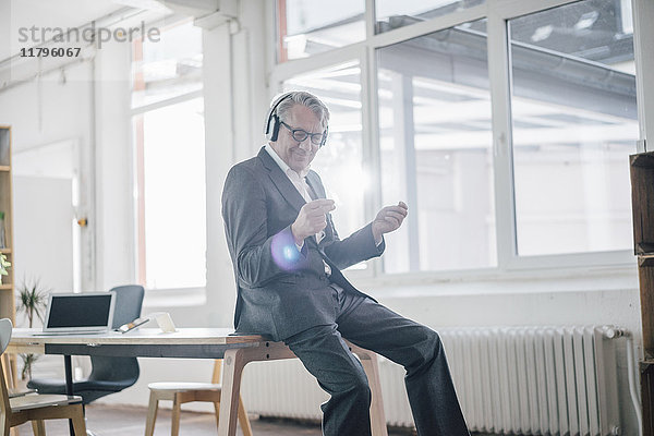 Glücklicher Senior-Geschäftsmann  der Musik mit Kopfhörern im Büro hört.