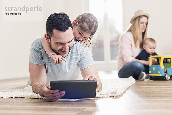 Vater und Tochter mit Tablette im neuen Zuhause mit Frau und Baby im Hintergrund