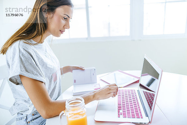 Junge Frau arbeitet zu Hause mit Laptop und Tablett