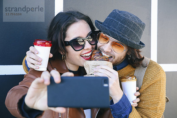 Junges Paar mit Croissant und Kaffee zum Mitnehmen mit Smartphone