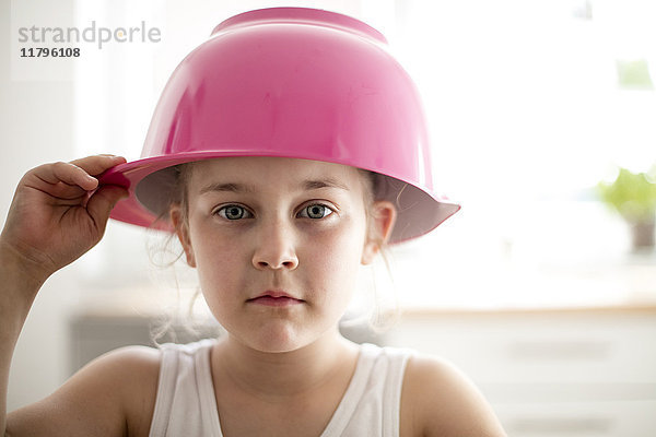 Porträt eines ernsthaften kleinen Mädchens mit rosa Rührschüssel auf dem Kopf