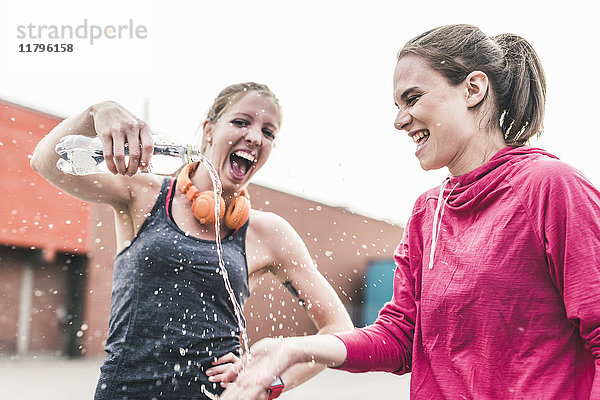 Zwei verspielte Frauen mit Wasserflasche  die eine Trainingspause einlegen.