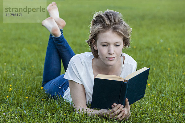 Barfuss junge Frau auf einer Wiese liegend  ein Buch lesend