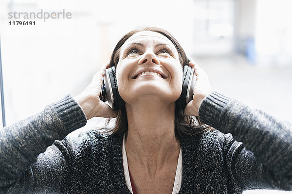 Porträt einer lächelnden Frau beim Musikhören mit Kopfhörer nach oben schauen