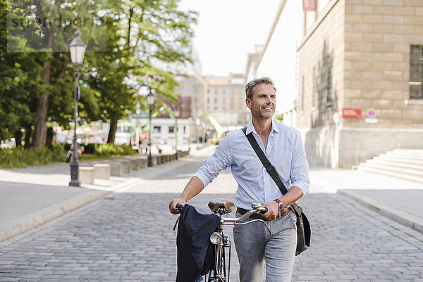 Lächelnder Mann schiebt Fahrrad in der Stadt