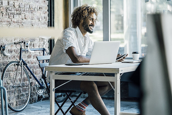 Lächelnder junger Mann am Schreibtisch mit Laptop