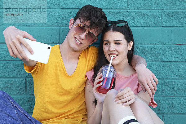 Junges Paar nimmt Selfie mit Smartphone vor blauer Ziegelwand