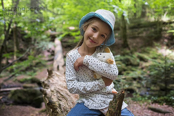 Porträt eines lächelnden Mädchens mit Kuscheltier im Wald