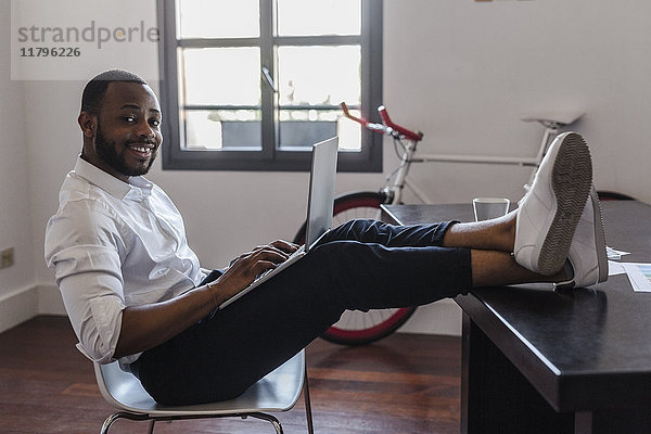 Mann mit Laptop im Home-Office mit Füßen auf dem Schreibtisch