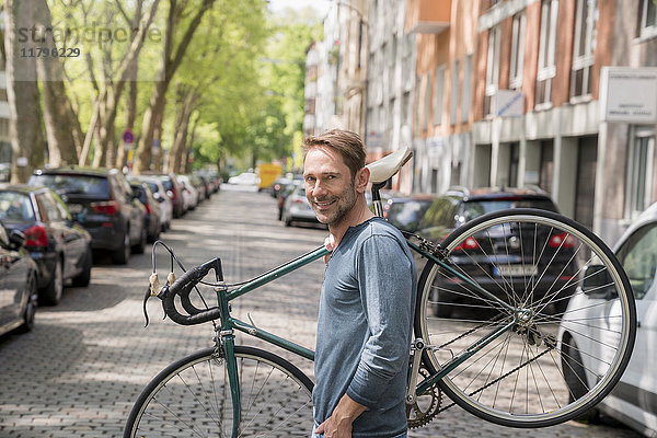 Porträt eines lächelnden  reifen Mannes  der sein Fahrrad auf der Schulter trägt.