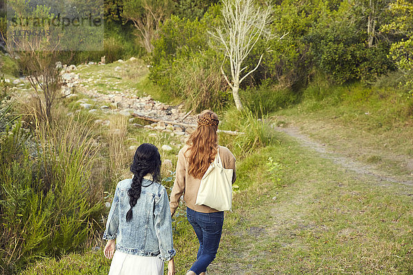 Rückansicht von zwei jungen Frauen  die in der Natur spazieren gehen.