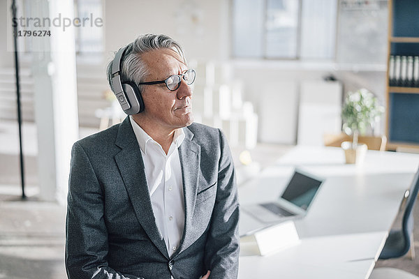 Senior Geschäftsmann beim Musikhören mit Kopfhörern im Büro