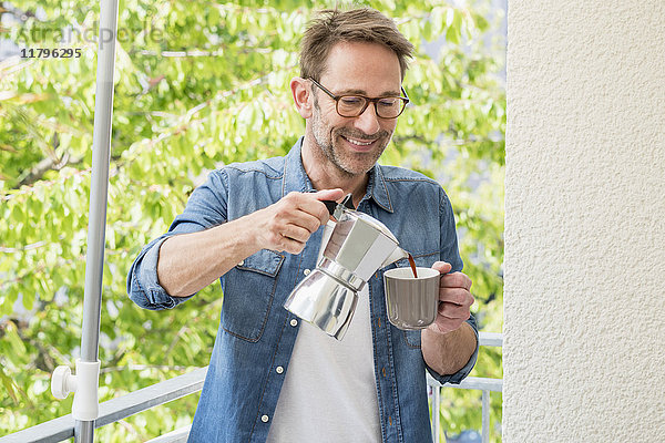 Lächelnder reifer Mann auf dem Balkon  der Kaffee in eine Tasse gießt.