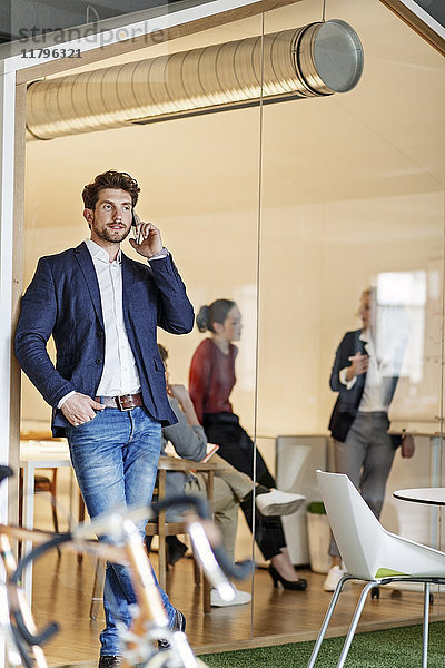 Geschäftsmann am Handy im Büro mit einer Besprechung im Hintergrund