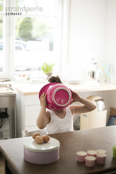 Kleines Mädchen in der Küche bedeckt ihr Gesicht mit rosa Rührschüssel