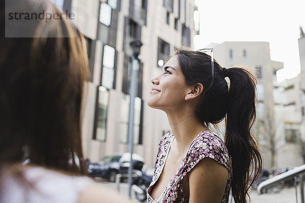 Lächelnde junge Frau in der Stadt schaut nach oben
