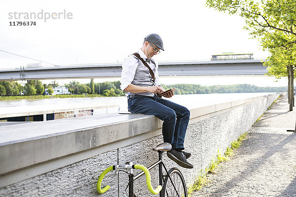 Geschäftsmann mit Fahrrad und Tablette am Flussufer