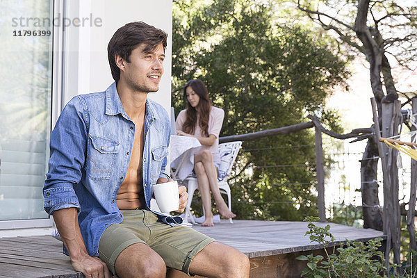 Mann auf der Terrasse mit Tasse Kaffee und Frau im Hintergrund