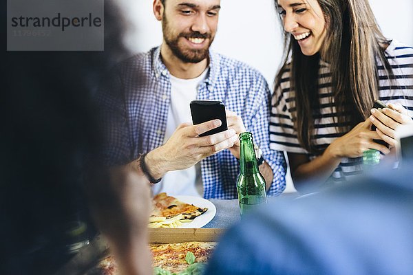 Ein glückliches Paar teilt sich sein Handy am Esstisch.