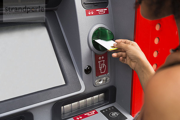 Frau schiebt Kreditkarte am Geldautomaten  Teilansicht