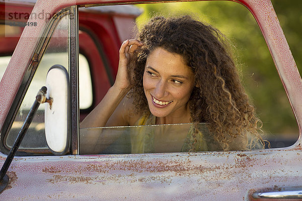 Fröhliche junge Frau  die ihr Haar im Autospiegel befestigt.