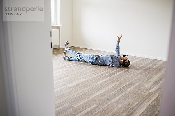 Mann auf dem Boden liegend in leerer Wohnung mit VR-Brille