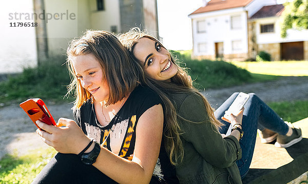 Zwei glückliche Mädchen mit ihren Smartphones im Freien