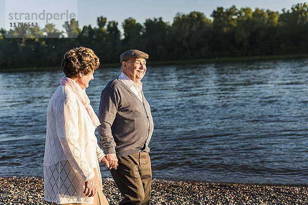 Glückliches Seniorenpaar  das Hand in Hand am Flussufer geht.