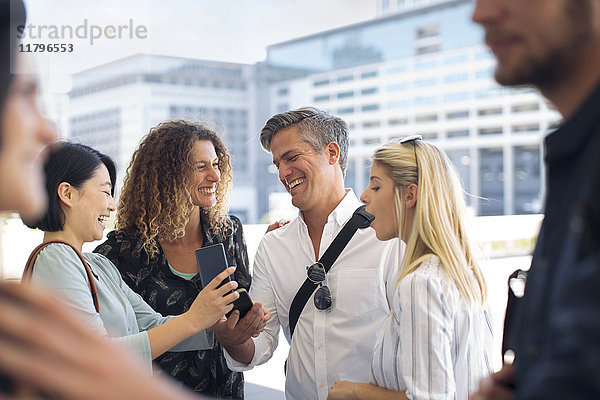 Gruppe von glücklichen Geschäftsleuten  die sich ein Handy auf dem Stadtplatz teilen.