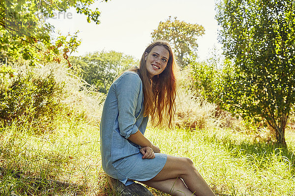 Porträt einer lächelnden jungen Frau auf einer Wiese sitzend