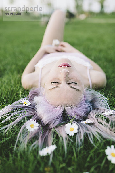 Frau auf Gras liegend mit Blumen auf Haaren