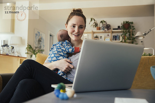 Mutter benutzt den Laptop und hält ihr neugeborenes Baby zu Hause.