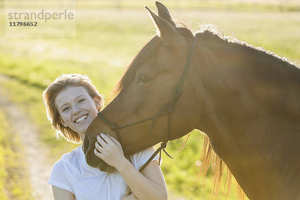 Porträt der glücklichen jungen Frau mit Pferd im Gegenlicht