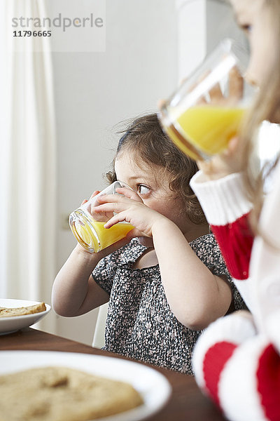 Kleine Mädchen trinken Orangensaft am Frühstückstisch