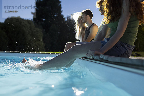 Vier Freunde sitzen in der Abenddämmerung Seite an Seite am Pool.