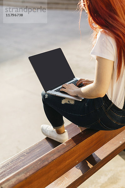 Rothaarige Frau auf der Bank sitzend mit Laptop