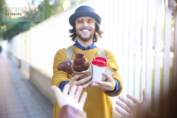 Junger Mann mit Croissant und Kaffee für die Straße