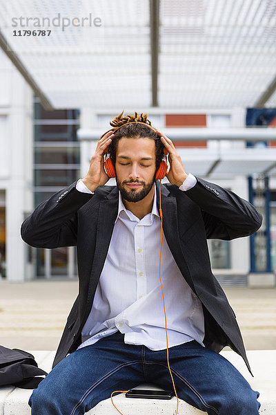 Portrait eines jungen Geschäftsmannes mit Dreadlocks beim Musikhören mit Kopfhörer und Handy