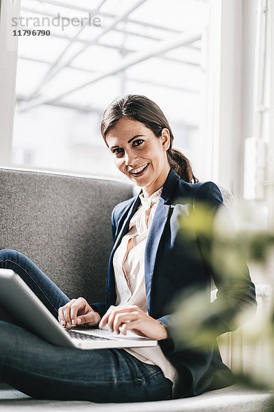 Portrait einer lächelnden Geschäftsfrau mit Laptop auf der Couch