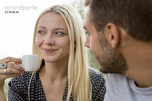 Porträt einer lächelnden blonden Frau mit Espressotasse  beobachtet von ihrem Freund.