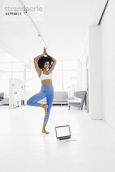 Junge Frau beim Yoga mit Laptop an der Seite