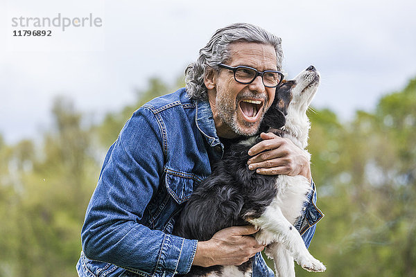 Porträt eines glücklichen älteren Mannes  der seinen Hund kuschelt.