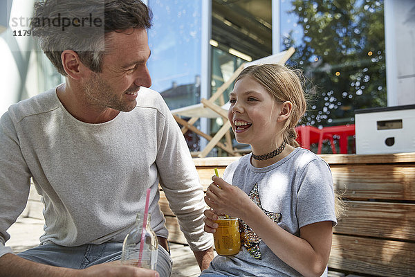 Glücklicher Vater und Tochter mit Getränken in einem Outdoor-Café