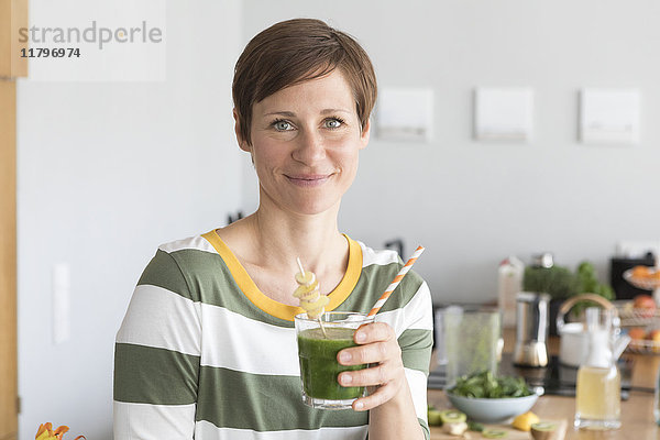 Porträt einer lächelnden Frau mit grünem Smoothie in der Küche