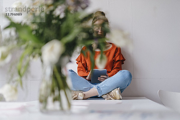 Junge Frau sitzt auf dem Tisch und benutzt eine mit Blumen bedeckte Tafel.
