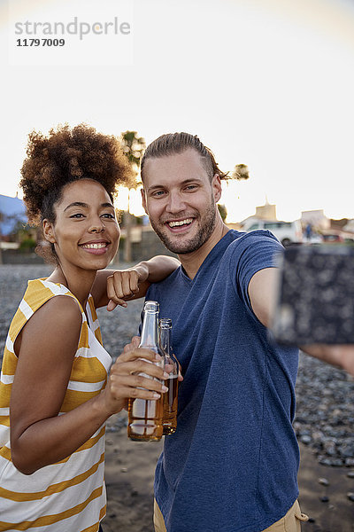 Zwei Freunde mit Bierflaschen  die Selfie am Strand mitnehmen.