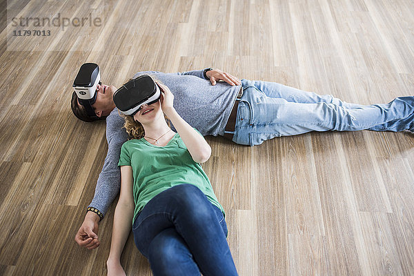 Junges Paar auf dem Boden liegend in leerer Wohnung mit VR-Brille